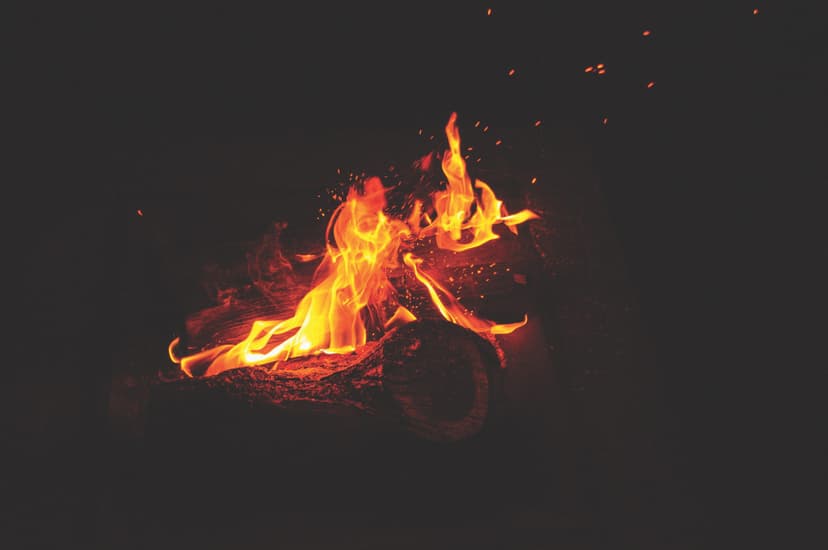 Bright orange and yellow flames dancing from burning logs with glowing embers and sparks against dark background