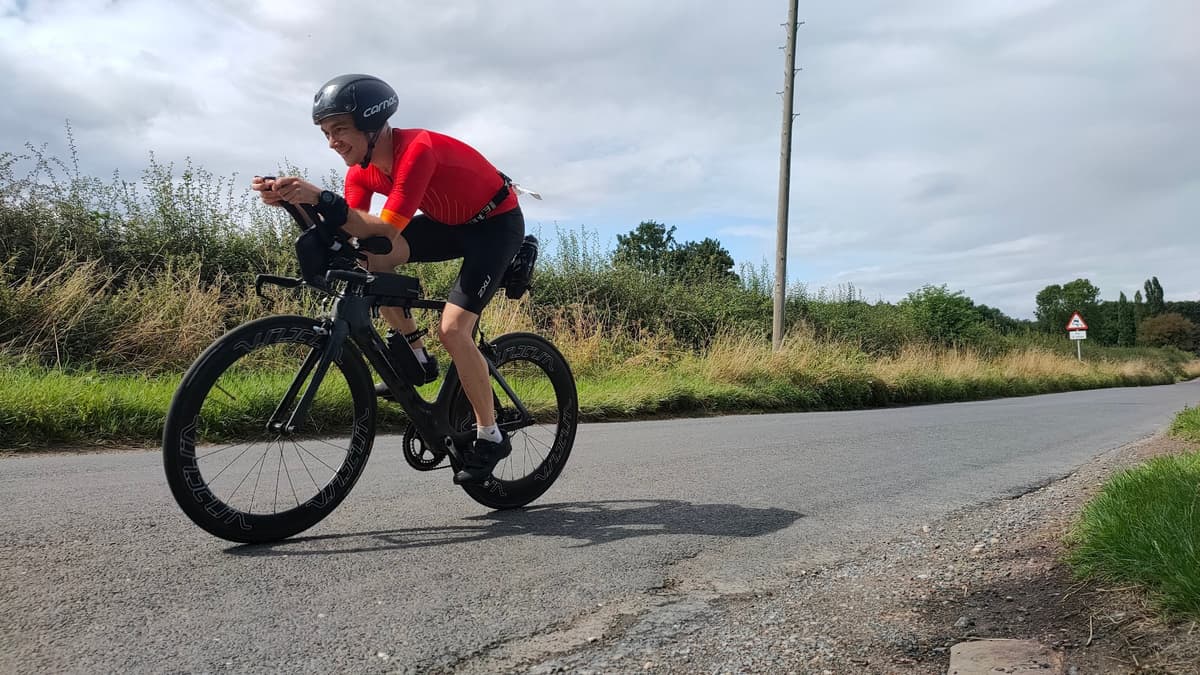 Triathlete in red jersey and aerodynamic helmet riding time trial bike on rural road with countryside vegetation