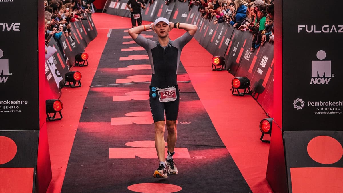 Triathlete crossing finish line with arms raised in celebration, wearing race number 2260, surrounded by cheering crowds and red event lighting