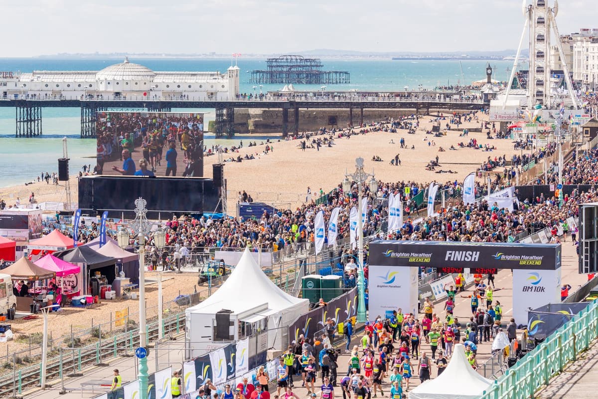 Runners crossing the finish line at Brighton Marathon with large crowds, Brighton Pier and seafront in background