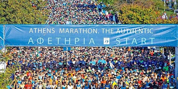 Hundreds of marathon runners gathered at the starting line beneath a blue "Athens Marathon, The Authentic" banner in Greece
